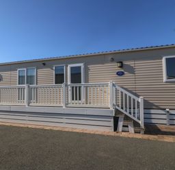 A beige mobile home with white railing and steps at Seafront Holiday Home 2 in Pwllheli