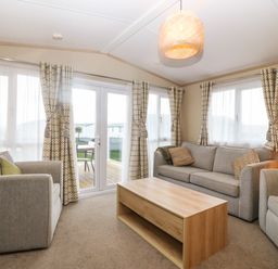 A living room with two armchairs a sofa a wooden coffee table and patterned curtains at Seafront Holiday Home 2 Pwllheli