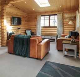 A living room with leather sofas armchairs a TV and a side table at Welcome Hjem Log Cabin Morpeth near Felton