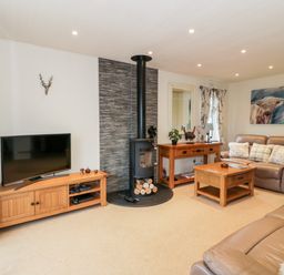 A living room with leather sofas wooden tables a television and a wood burning stove at Eden Lodge in Castlewigg near Whithorn