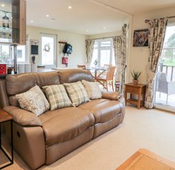 A living room with a leather sofa and pillows near a sliding glass door and dining area at Eden Lodge Castlewigg near Whithorn