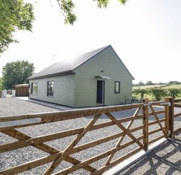 A single story house with green siding behind a wooden gate on a gravel driveway at Southend in Welland