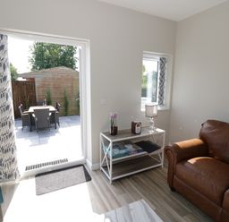 Living room with brown leather sofa blue chair white table with lamp and board games and patio door opening to outdoor dining area at Southend in Welland