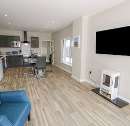 A room with kitchen and dining area including black chairs and a blue armchair and a wall mounted TV at Southend in Welland
