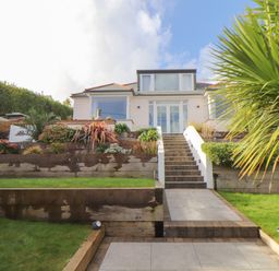 A house with stairs leading up to a patio garden with plants and lawn at Higher Bolenna in Perranporth