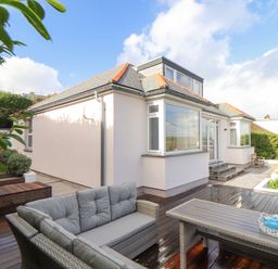 An outdoor patio with wicker sofa and table with tea set next to a house with large windows at Higher Bolenna in Perranporth