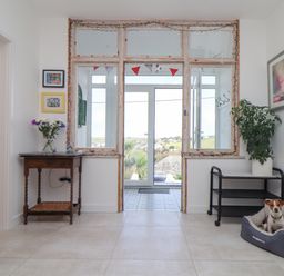A hallway with a wooden table with flowers on the left a plant on a black metal cart on the right and a dog in a bed at Higher Bolenna in Perranporth
