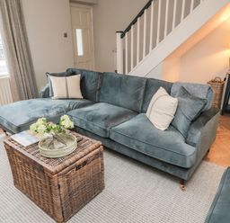 A living room with a blue sectional sofa and a wicker coffee table at Driftwood Sands in Beadnell