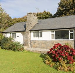A stone and white exterior cottage with a large chimney and garden with flowers and shrubs at Ty Cerrig in Llanbedrog