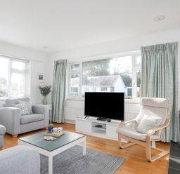 A living room with two armchairs a TV on a stand a coffee table and large windows with curtains at Ty Cerrig in Llanbedrog