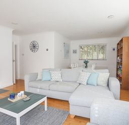 A living room with a gray sectional sofa a coffee table and a dining area in the background at Ty Cerrig in Llanbedrog