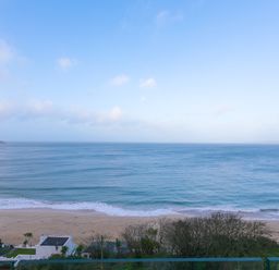 A beach with waves and a few buildings and trees near the shore at Wavetop in Carbis Bay
