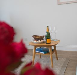 A small wooden table with a bottle of champagne two empty glasses a bowl of snacks and a plate of sushi in a living room at Wavetop in Carbis Bay