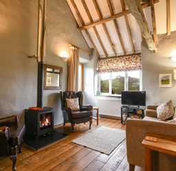A living room with wooden beams two armchairs a sofa a wood burning stove and a television at The Old Dairy Whitchurch Canonicorum near Charmouth