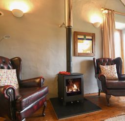 A sitting area with two leather armchairs a wood stove and a window with curtains at The Old Dairy in Whitchurch Canonicorum near Charmouth