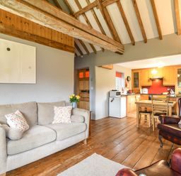 A living room with a beige sofa and wooden table connected to a kitchen with wooden cabinets and dining table at The Old Dairy Whitchurch Canonicorum near Charmouth