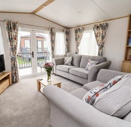 A living room with grey sofas a wooden TV stand a coffee table with flowers and a bookshelf at Silverdale View in East Heslerton near Sherburn