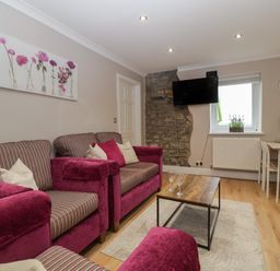 A living room with pink armchairs a wooden coffee table a wall-mounted TV and a dining table at Myrtle Cottage in St Brides-Super-Ely