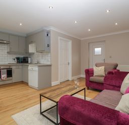 A living area with purple sofas and a wooden coffee table beside a kitchen with grey cabinets and white appliances at Myrtle Cottage in St Brides-Super-Ely