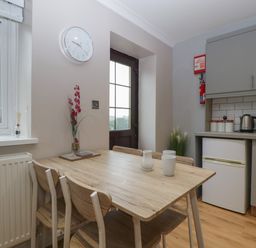 A kitchen with a wooden dining table and chairs near a window and a door at Myrtle Cottage in St Brides-Super-Ely