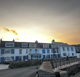 A row of houses with blue and white shutters near a stone wall and a car on the street at Waves End in Mevagissey
