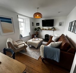 A living room with a brown sofa and armchair a window with shutters and a wall-mounted TV at Waves End Mevagissey