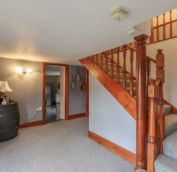 A hallway with carpeted stairs and wooden banister and a black barrel serving as table with a lamp and decor at High Shaftoe in Ponteland