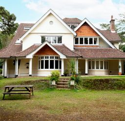 A large house with a tiled roof and covered porch on a grassy lawn with a picnic table