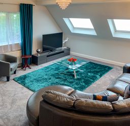 A living room with a curved leather sofa a glass coffee table a TV on a stand and teal curtains at The Gables Penthouse in Bournemouth