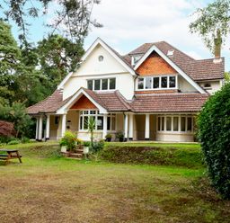 A large two story house with a porch and tiled roof surrounded by trees and a lawn with a picnic table at The Gables Penthouse in Bournemouth
