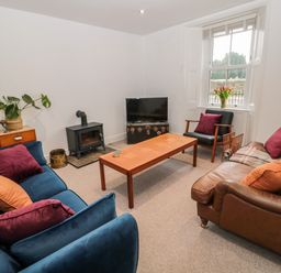 A living room with sofas a wooden coffee table a television and a window with flowers at Tyne View Cottage in Bellingham
