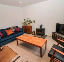 A living room with a blue sofa a brown armchair a wooden coffee table a black wood stove a television and a wooden cabinet at Tyne View Cottage in Bellingham