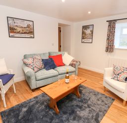 A living room with a sofa chairs wooden coffee table and framed pictures on wall at The Byre in Carrshield near Allendale