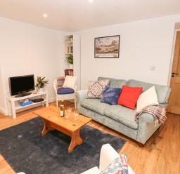 A living room with a sofa bed with several cushions a wooden coffee table with a bottle and glasses a small television on a white stand and a white armchair at The Byre in Carrshield near Allendale