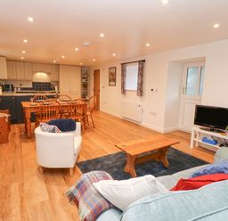 An open plan living and dining room with a sofa a coffee table a television dining table with chairs and a kitchen at The Byre in Carrshield near Allendale