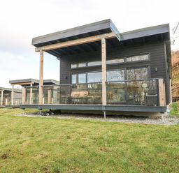 A row of modern cabins with glass balconies on a grassy hillside at Coorie In in Aberfeldy
