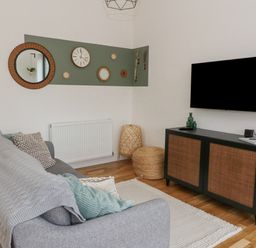 A living room with a gray sofa a wall-mounted television and a cabinet at Coorie In Aberfeldy