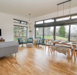 A living room and dining area with wooden floor large windows and green chairs at Coorie In Aberfeldy