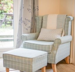 A chair with a matching ottoman and a window with floral curtains at The Old Lace Shop in Beer