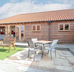 An outdoor patio area with a wooden bench and a table with three chairs in front of a wooden building at 5a Hideaways in Hunstanton