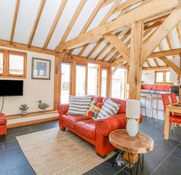 A living area with a red leather sofa and chair wooden beams and a dining table with red chairs at 5a Hideaways in Hunstanton