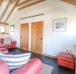 A living room with red leather sofas wooden doors and beams and a wall-mounted television at 5a Hideaways in Hunstanton