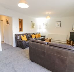 A living room with brown leather sofas and yellow cushions a wooden coffee table a television on a wooden stand and framed pictures on walls at Borthwen in Barmouth