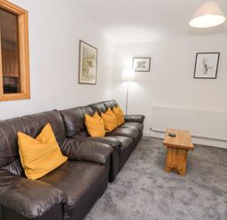 A living room with a dark leather sofa with orange cushions a wooden coffee table and framed pictures on the walls at Borthwen in Barmouth