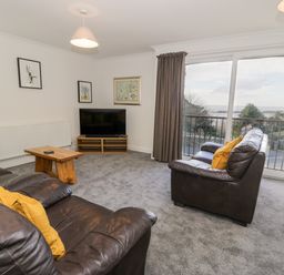 A living room with leather sofas and yellow cushions a wooden coffee table and a television by a sliding glass door at Borthwen in Barmouth