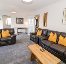 A living room with two brown leather sofas with yellow cushions a wooden coffee table and a wooden desk against the wall at Borthwen in Barmouth