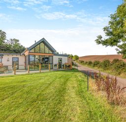 A house with large windows and a glass railing on a grassy lawn next to a rural road at Shearwater Lodge Bamburgh