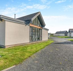 A cluster of modern single story houses with large windows and a gravel road at Shearwater Lodge in Bamburgh