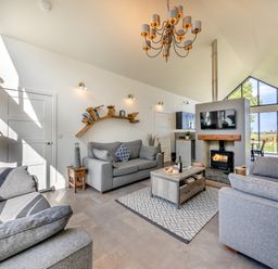 A living room with grey sofas a coffee table and a fireplace with a TV above at Shearwater Lodge in Bamburgh