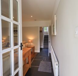 A hallway with a wooden table and lamp leading to a living room and staircase inside Brook Cottage in Windermere